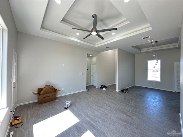 empty room with a raised ceiling, wood finished floors, visible vents, and baseboards