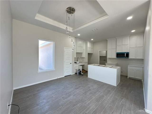 kitchen with dark wood finished floors, stainless steel microwave, and a raised ceiling