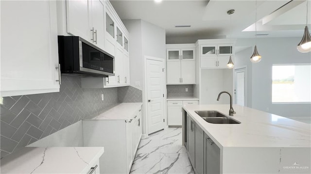 kitchen with pendant lighting, light stone counters, white cabinetry, and sink