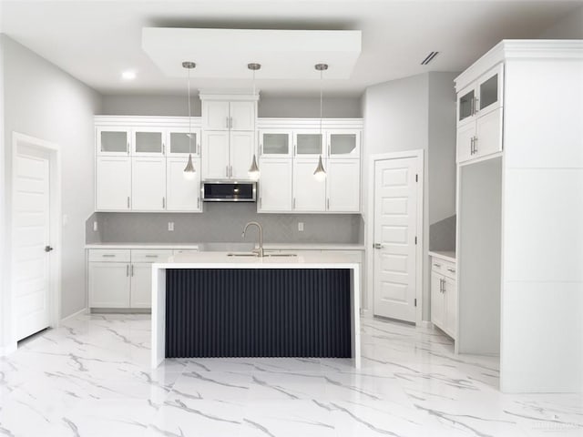 kitchen with pendant lighting, white cabinets, sink, and a kitchen island with sink