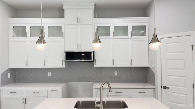 kitchen with light stone counters, white cabinetry, and sink