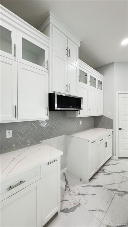 kitchen featuring light stone counters, white cabinetry, and backsplash