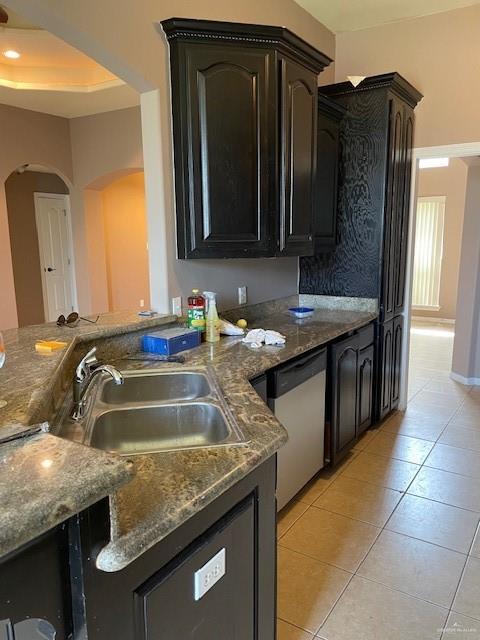 704 N Drennan St N, Edinburg, TX 78541 - kitchen featuring stainless steel dishwasher, arched walkways, light tile patterned floors, a sink, and dark stone countertops