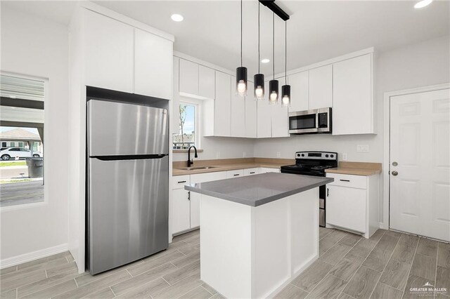 kitchen with sink, stainless steel appliances, a center island, white cabinets, and decorative light fixtures