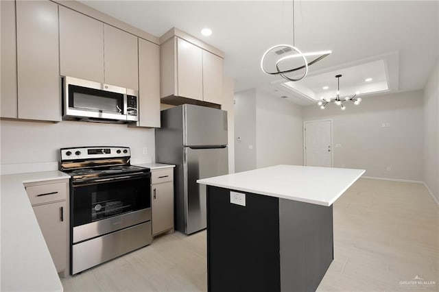 kitchen with an inviting chandelier, decorative light fixtures, a center island, appliances with stainless steel finishes, and a raised ceiling