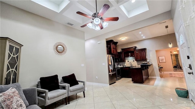 living room featuring coffered ceiling, a skylight, ceiling fan, a towering ceiling, and light tile patterned floors