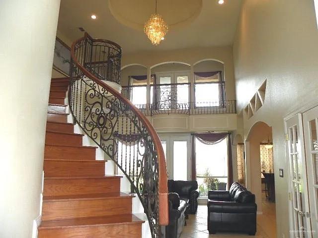 staircase with french doors, a towering ceiling, a chandelier, and tile patterned flooring