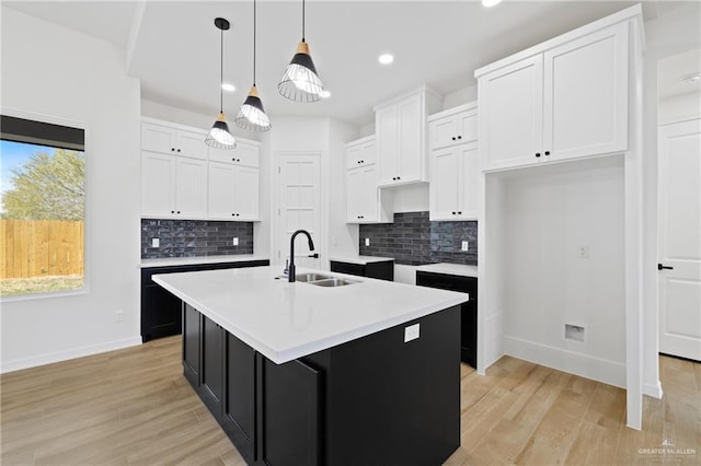 kitchen with sink, a kitchen island with sink, white cabinetry, light hardwood / wood-style floors, and decorative light fixtures