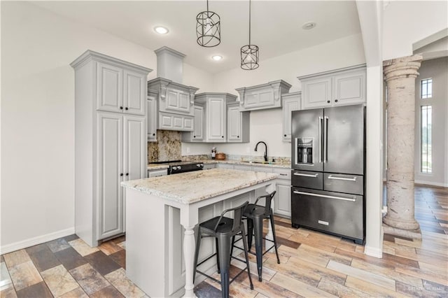 kitchen featuring ornate columns, sink, a kitchen breakfast bar, high end fridge, and a kitchen island