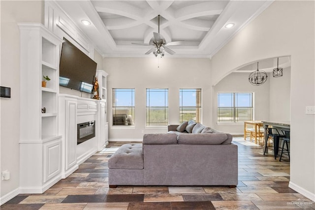 living room with ceiling fan with notable chandelier, dark wood-type flooring, coffered ceiling, and ornamental molding