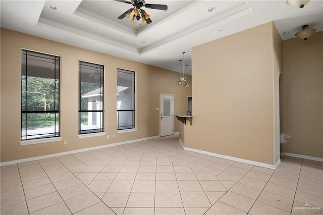 empty room with a raised ceiling, ceiling fan, and light tile patterned floors