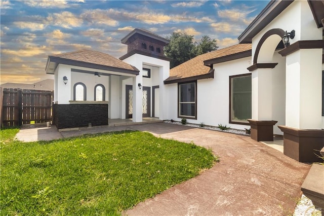 exterior space with a front lawn, roof with shingles, stucco siding, and fence