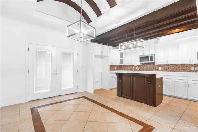 kitchen featuring light countertops, decorative backsplash, stainless steel microwave, and white cabinets