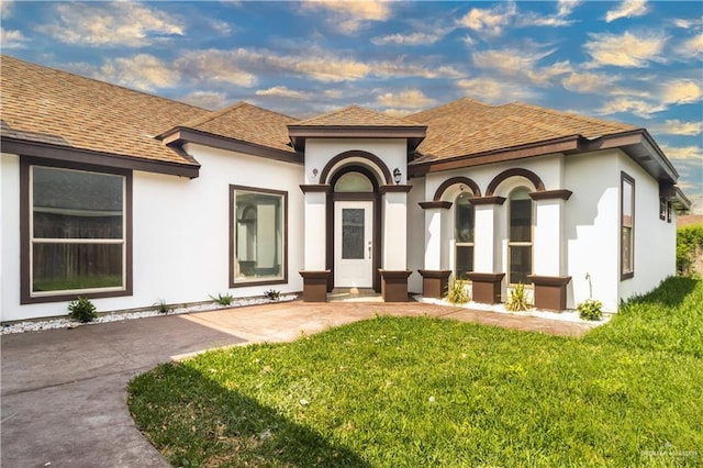 view of front of property featuring stucco siding, roof with shingles, and a front lawn