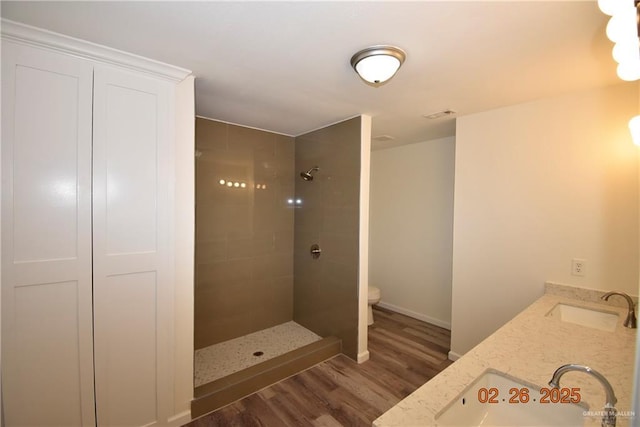 full bathroom featuring toilet, wood finished floors, a tile shower, and a sink