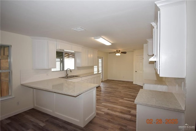 kitchen with light stone counters, visible vents, a peninsula, a sink, and white cabinets