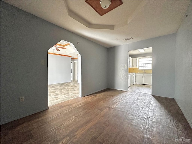 empty room with hardwood / wood-style flooring, ceiling fan, a raised ceiling, and sink