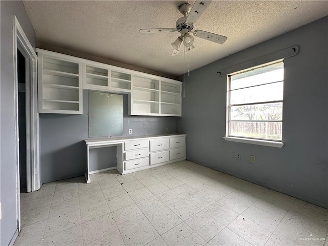 unfurnished office featuring ceiling fan, built in desk, and a textured ceiling