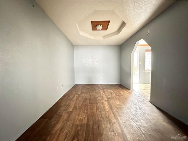 unfurnished room featuring a tray ceiling, hardwood / wood-style floors, and a textured ceiling