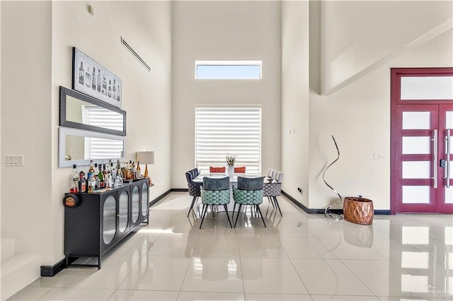 dining area with a towering ceiling, light tile patterned floors, and baseboards