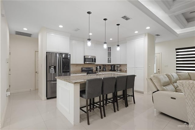 kitchen with light stone counters, an island with sink, pendant lighting, stainless steel appliances, and white cabinets