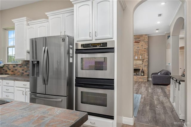 kitchen featuring white cabinetry, tile counters, dark hardwood / wood-style floors, appliances with stainless steel finishes, and ornamental molding