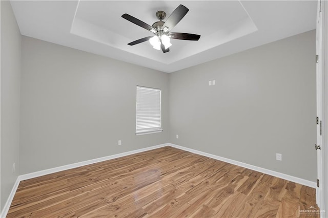 unfurnished room featuring light wood-style flooring, baseboards, and a raised ceiling