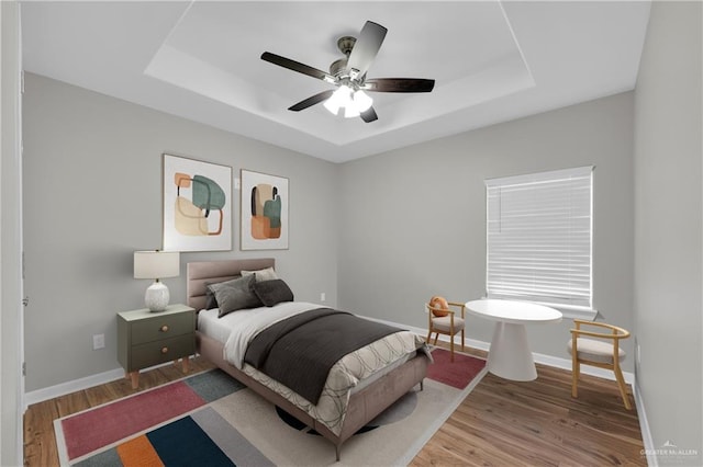 bedroom with baseboards, wood finished floors, and a raised ceiling