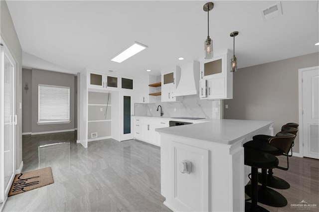 kitchen with a peninsula, premium range hood, light countertops, visible vents, and a kitchen bar