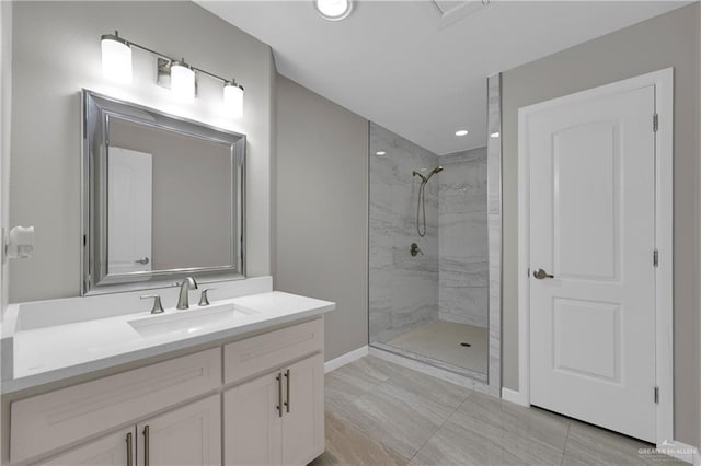 bathroom with a tile shower, vanity, and baseboards