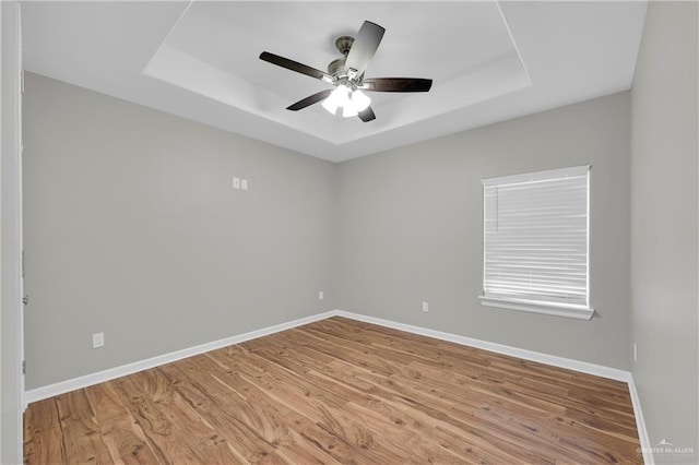 unfurnished room featuring a raised ceiling, ceiling fan, baseboards, and light wood-style flooring
