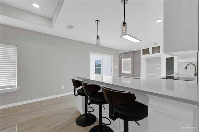 kitchen featuring a peninsula, white cabinetry, visible vents, a sink, and baseboards