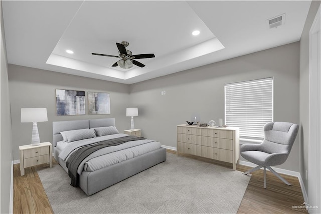 bedroom with a tray ceiling, light wood-type flooring, baseboards, and visible vents
