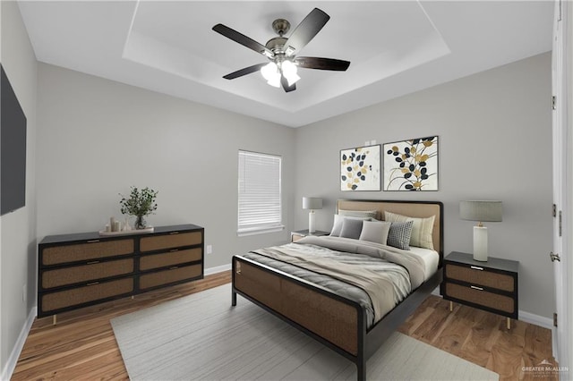 bedroom featuring baseboards, wood finished floors, a ceiling fan, and a raised ceiling