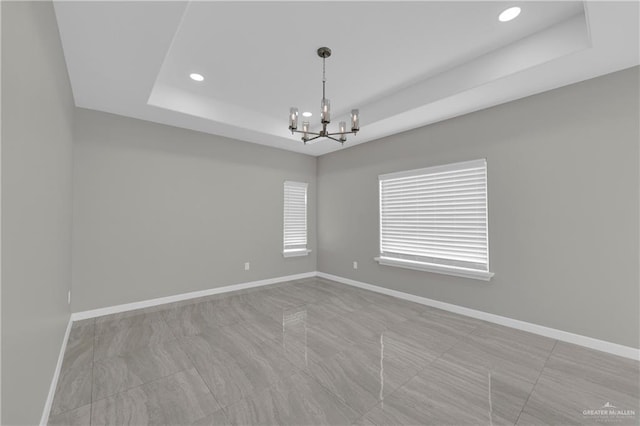 empty room featuring baseboards, recessed lighting, a tray ceiling, and an inviting chandelier