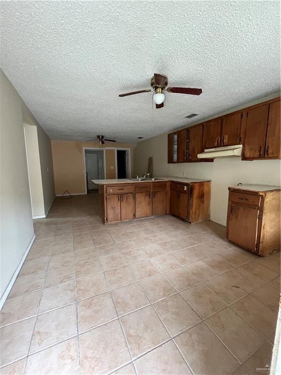 2322 E La Pointe Ave, Alton, TX 78573 - kitchen with a ceiling fan, under cabinet range hood, light tile patterned flooring, a peninsula, and a textured ceiling