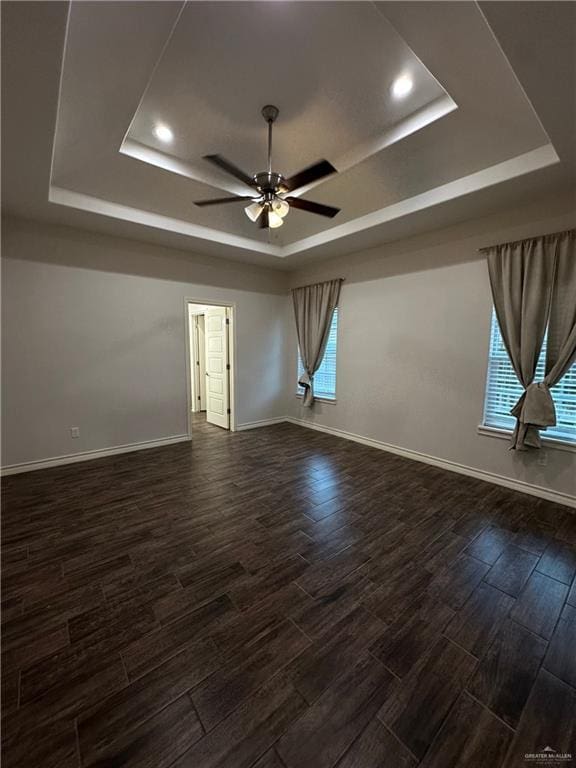 unfurnished room with dark hardwood / wood-style flooring, a tray ceiling, and ceiling fan