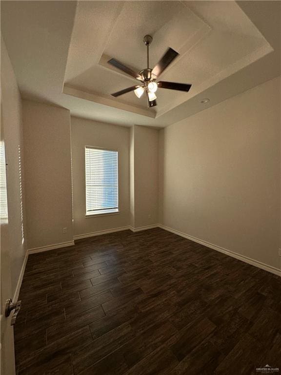 empty room featuring ceiling fan, dark wood-type flooring, and a tray ceiling