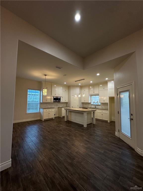 kitchen with a kitchen island, white cabinetry, hanging light fixtures, and dark wood-type flooring