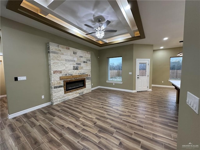 unfurnished living room with a tray ceiling, ceiling fan, and a stone fireplace