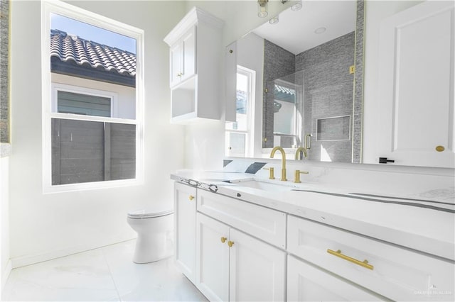 bathroom with a tile shower, plenty of natural light, vanity, and toilet