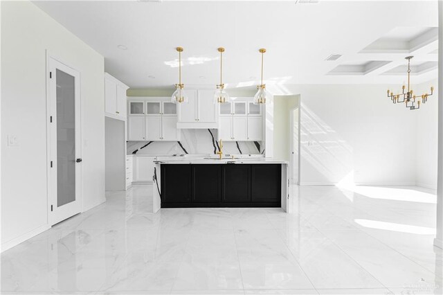 kitchen with a notable chandelier, coffered ceiling, a center island with sink, decorative light fixtures, and white cabinetry