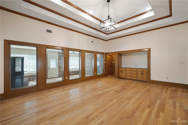 interior space with a raised ceiling, ornamental molding, a notable chandelier, and light hardwood / wood-style floors