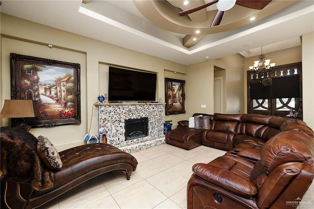 living room with light tile patterned floors, ceiling fan with notable chandelier, and a raised ceiling