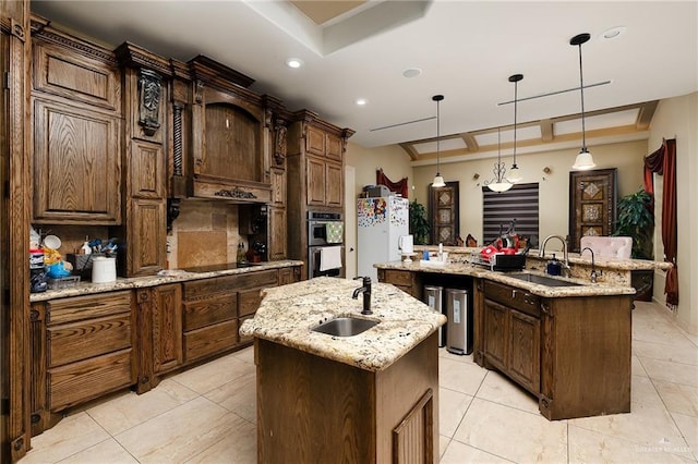 kitchen with a tray ceiling, sink, pendant lighting, a center island with sink, and white fridge