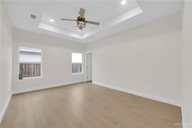 unfurnished room with ceiling fan, a tray ceiling, and light hardwood / wood-style floors