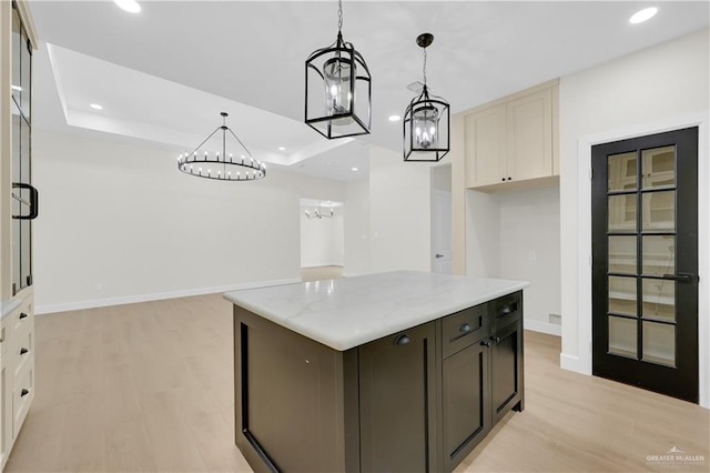 kitchen with light stone counters, hanging light fixtures, a kitchen island, and light wood-type flooring