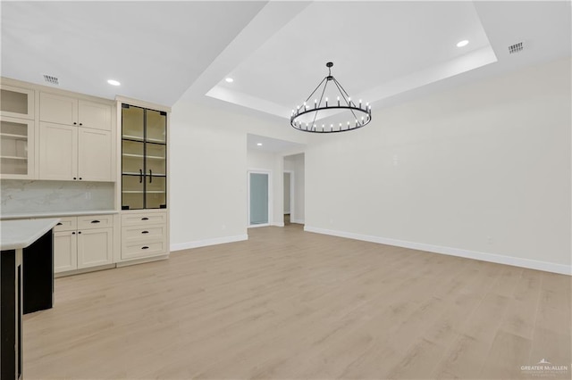 unfurnished living room with a tray ceiling, light hardwood / wood-style flooring, and a notable chandelier