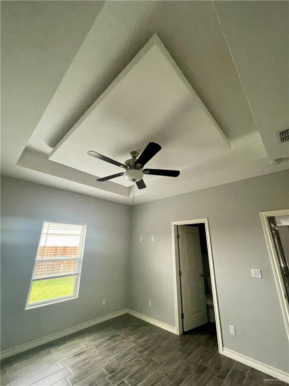 unfurnished room with ceiling fan, a raised ceiling, and dark wood-type flooring