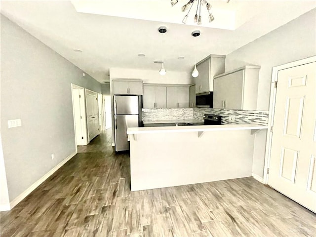 kitchen with tasteful backsplash, kitchen peninsula, hardwood / wood-style flooring, and appliances with stainless steel finishes